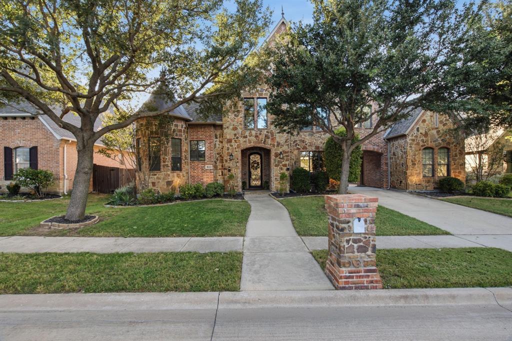 Stone and brick exterior facade, turret-style architectural element, arched entryway, concrete driveway, and mature landscaping