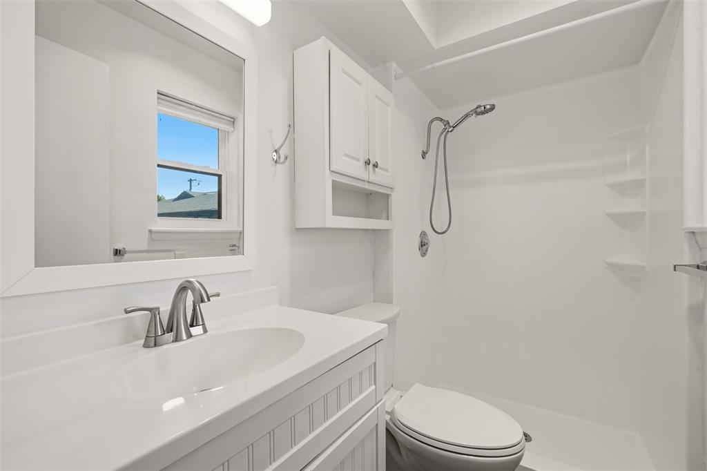 Spa-inspired bathroom featuring a floating vanity with quartz countertop and chrome faucet, white subway tile surround, frameless glass-enclosed shower with rainfall showerhead, toilet with elongated bowl, recessed medicine cabinet, and natural light from a picture window