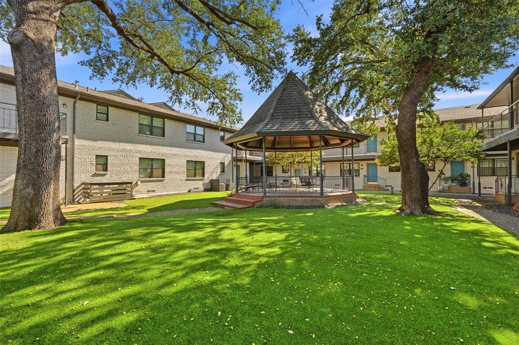 Lush green lawn with mature trees, a central gazebo with a shingled roof, and brick-clad buildings