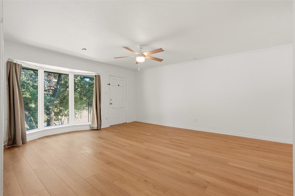 Expansive room featuring wood-finish flooring, a bay window, a ceiling fan with integrated lighting, and a white paneled door