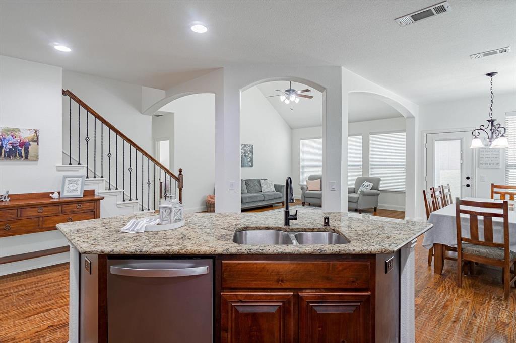 Kitchen island with a double basin sink, stainless steel dishwasher, and stone-finish countertop
