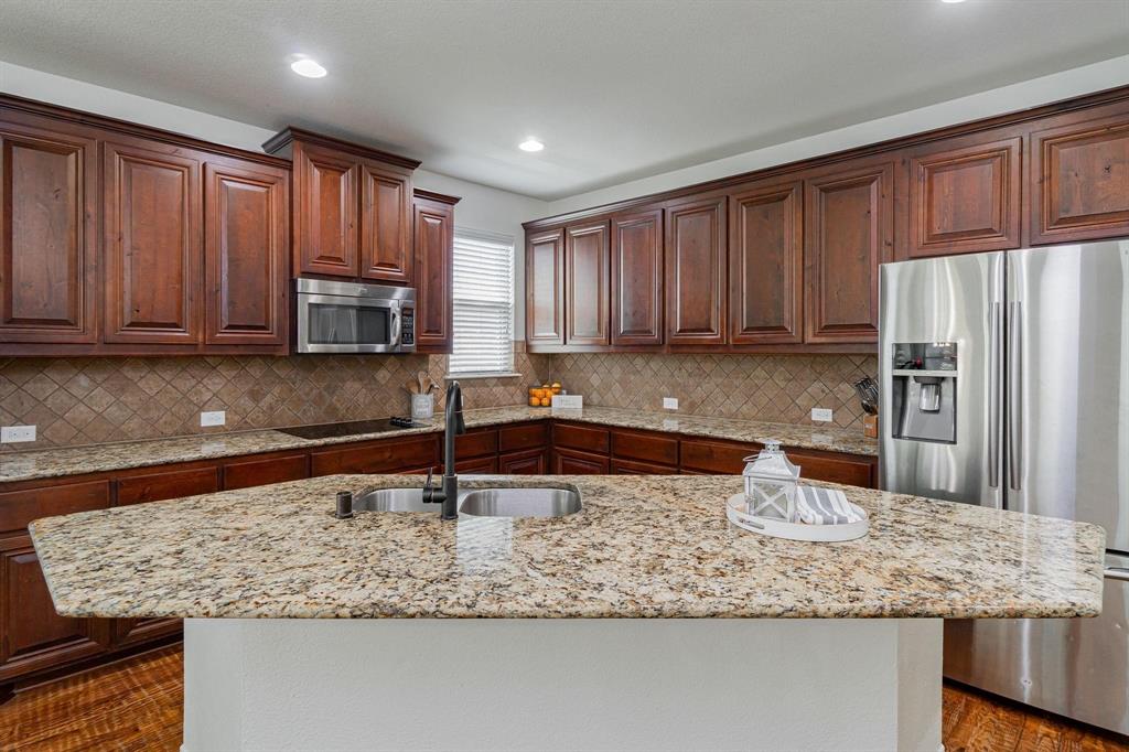 Kitchen featuring a large island with a double basin sink, stainless steel appliances, wood-finish cabinetry, and tiled backsplash