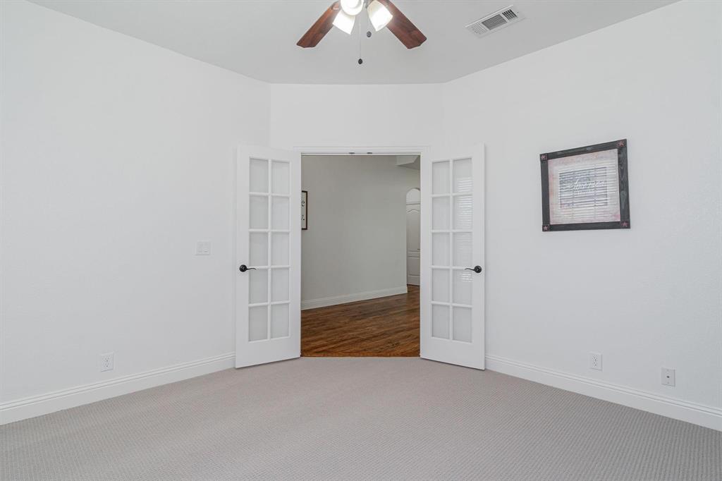 Light-colored carpeting with white baseboards, a ceiling fan with light fixture, and French doors