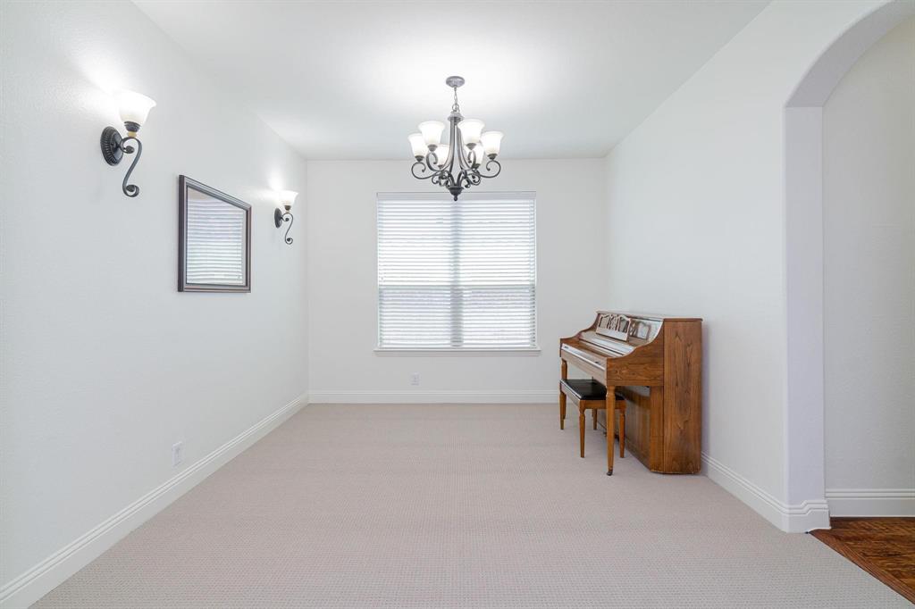 Recessed window with blinds, wrought iron chandelier, wall sconces, arched doorway, and carpeted flooring