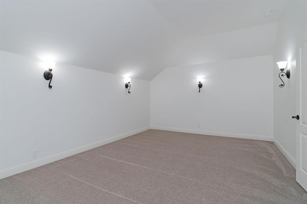Sloped ceiling room featuring carpet flooring, crisp white walls, and decorative wall sconces
