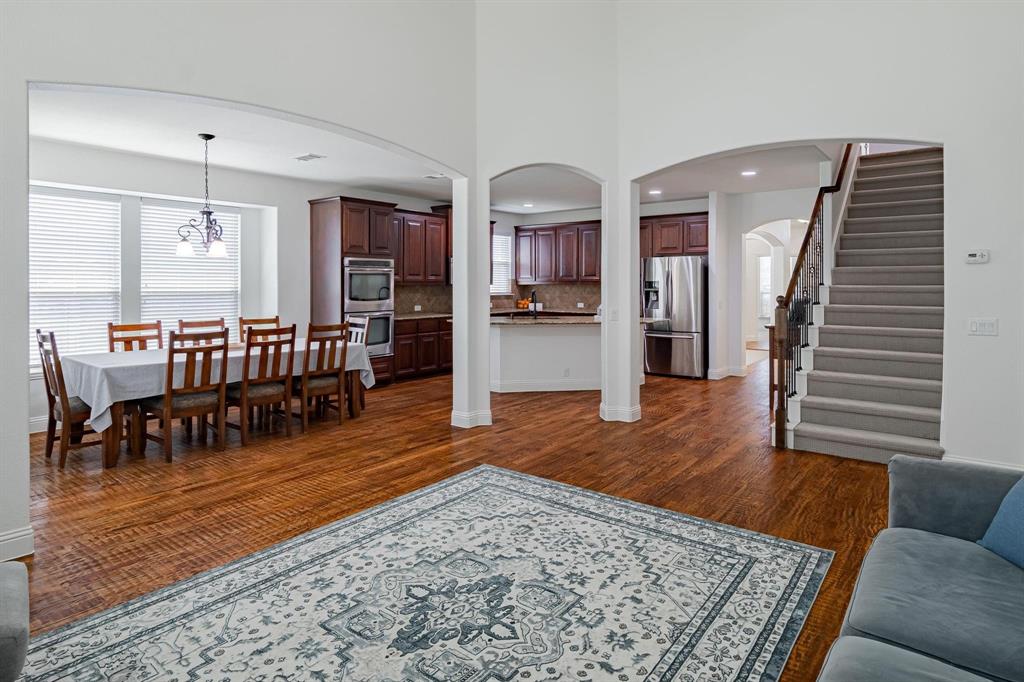 Arched doorways, wood-finish flooring, staircase with carpeted treads, dark wood cabinetry, and stainless steel appliances