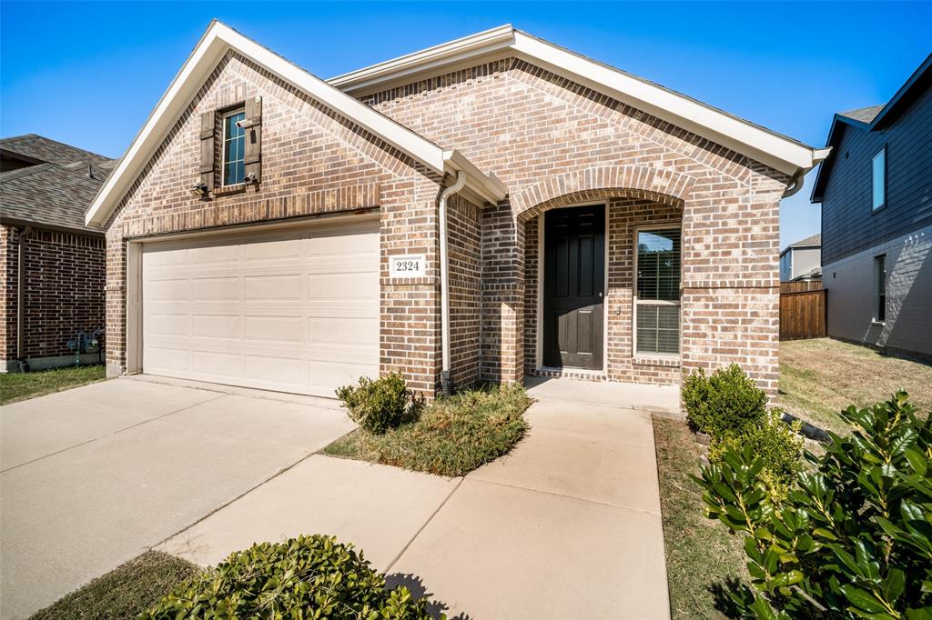 Brick exterior featuring a gabled roofline, recessed arched entryway, two-car garage, and low-maintenance landscaping Brick exterior featuring a gabled roofline, recessed arched entryway, two-car garage, and low-maintenance landscaping