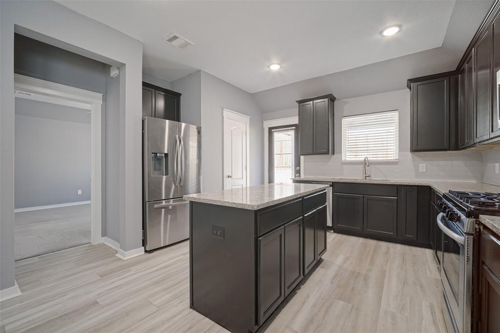 Kitchen featuring dark cabinetry, stone-surface countertops, central island, stainless steel appliances, and wood-finish flooring