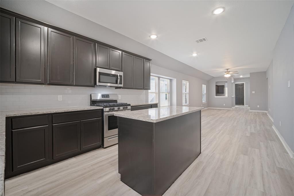 Kitchen featuring dark cabinetry, stone-finish countertops, stainless steel appliances, a subway tile backsplash, and wood-finish flooring