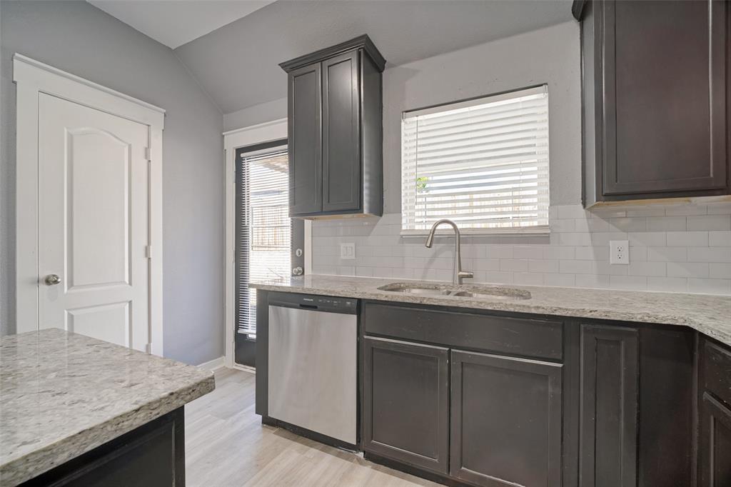 Kitchen featuring dark cabinetry, stone-finish countertops, stainless steel dishwasher, white subway tile backsplash, and a stainless steel faucet