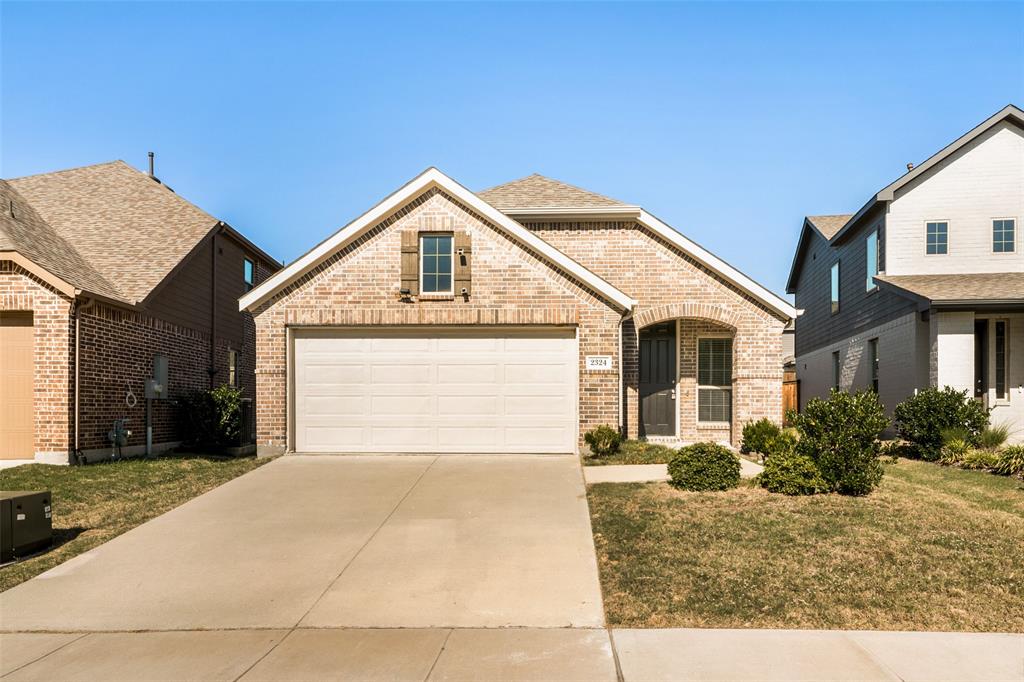 Single-story brick exterior featuring a gable roofline, an attached two-car garage, and decorative shutters Single-story brick exterior featuring a gable roofline, an attached two-car garage, and decorative shutters