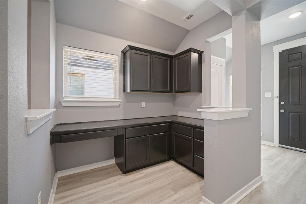 Built-in dark cabinetry with lower storage drawers, integrated desk surface, and wood-finish flooring Built-in dark cabinetry with lower storage drawers, integrated desk surface, and wood-finish flooring