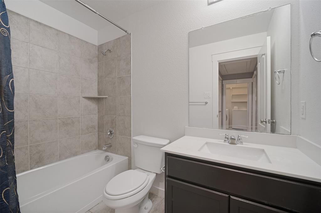 Bathroom featuring a vanity with a white countertop and rectangular undermount sink, dark-toned cabinetry, a full-width wall-mounted mirror, and a tub with large-format stone-style wall tile