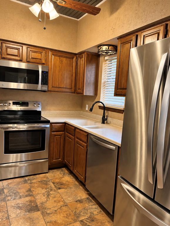 Kitchen featuring stainless steel appliances, wood cabinetry, light-toned countertops, and patterned tile flooring
