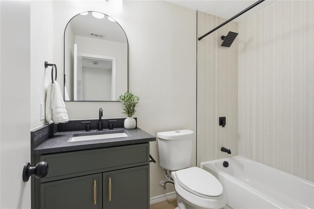Dark cabinetry featuring a solid surface countertop, rectangular under-mount sink, arched mirror, and matte black hardware including a square shower head and faucet