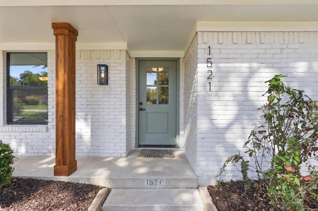 Exterior featuring a painted brick facade, covered entryway with a wood-finished pillar, four-panel glass-inset entry door, and dark-framed wall-mounted lighting Exterior featuring a painted brick facade, covered entryway with a wood-finished pillar, four-panel glass-inset entry door, and dark-framed wall-mounted lighting