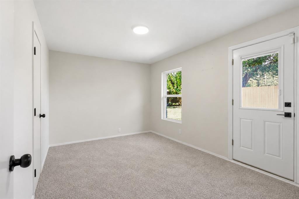 Neutral-toned interior space featuring carpeting, a white entry door with an integrated glass panel, a single window, and matte black door hardware