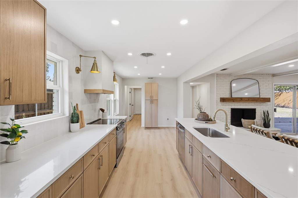 Kitchen featuring light wood-finish cabinetry, quartz countertops, a central island with an undermount sink, recessed lighting, and a painted brick fireplace with a wood mantel