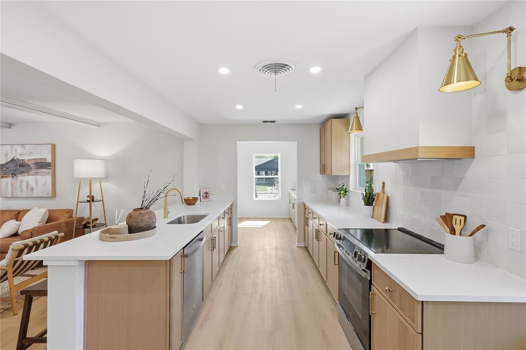 Kitchen featuring light wood-finish cabinetry, white solid-surface countertops, subway-style tile backsplash, stainless steel appliances, and brass-finish wall-mounted lighting Kitchen featuring light wood-finish cabinetry, white solid-surface countertops, subway-style tile backsplash, stainless steel appliances, and brass-finish wall-mounted lighting
