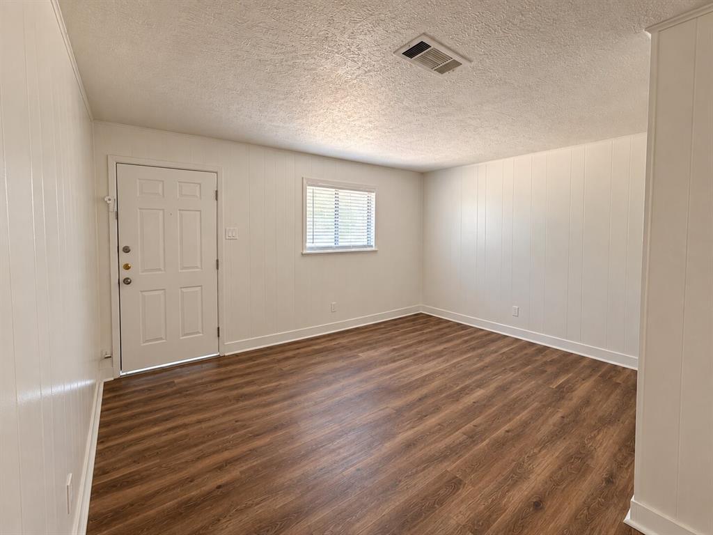 Wood-finish flooring with white baseboards, vertical paneling, and a panel door with multiple lites