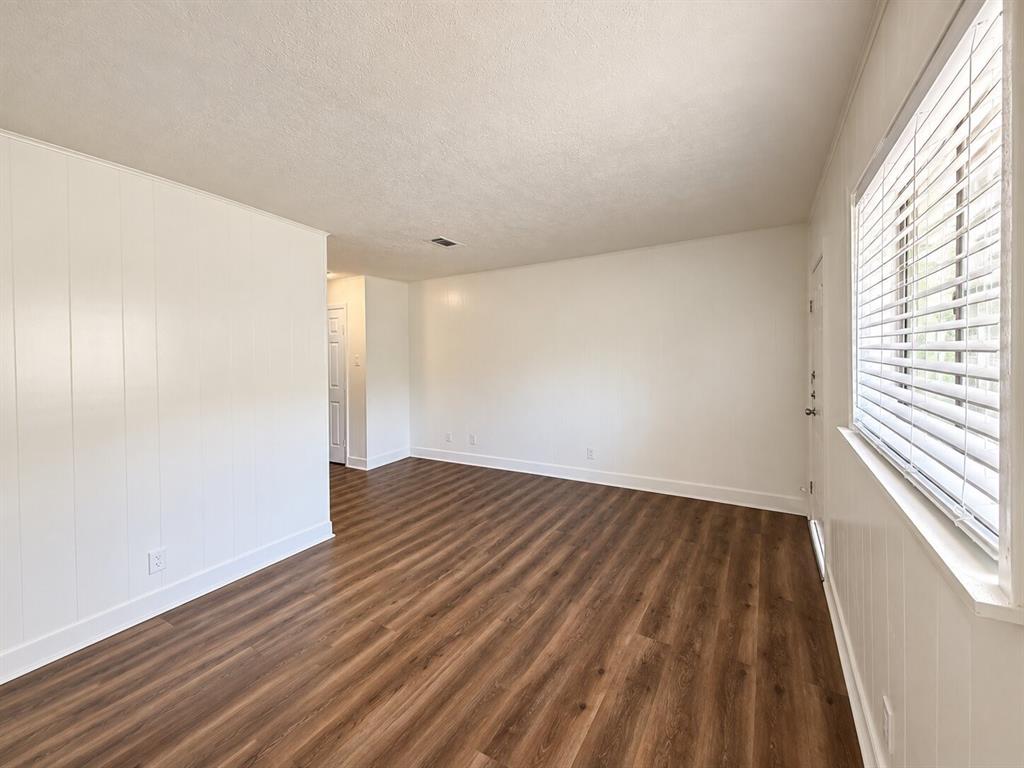 Wood-finish flooring, white paneled accent wall, white window blinds, and white trim throughout