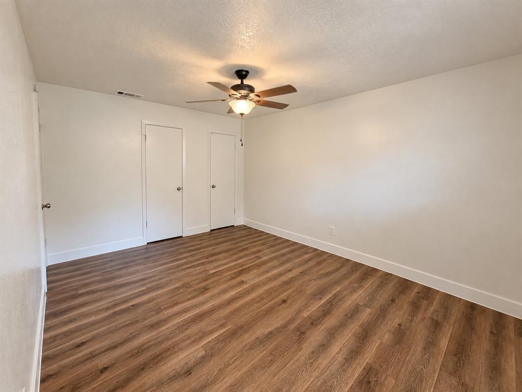 Wood-finish flooring, ceiling fan with integrated lighting, two white panel doors, and neutral wall tones Wood-finish flooring, ceiling fan with integrated lighting, two white panel doors, and neutral wall tones