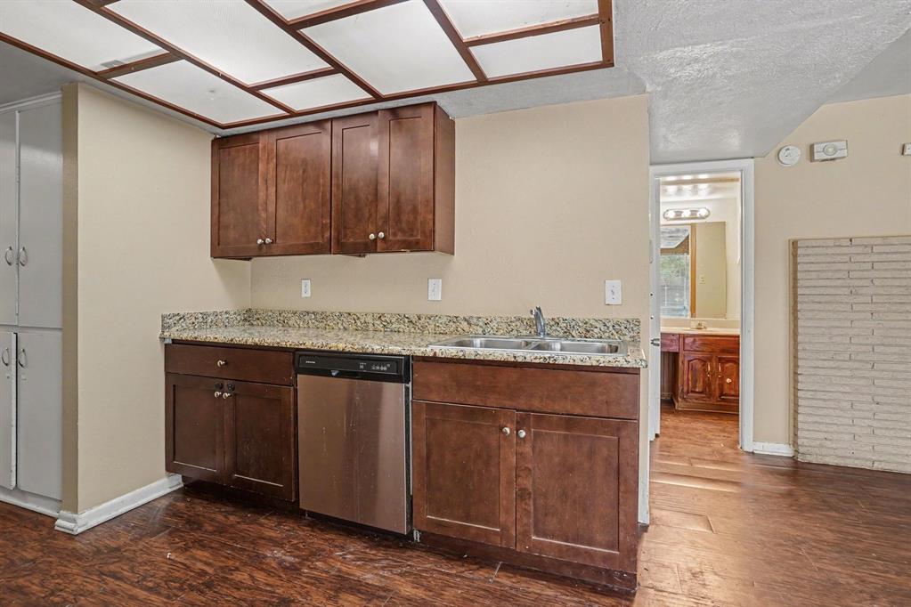 Kitchenette featuring dark wood cabinetry, granite-style countertops, stainless steel dishwasher, and a double basin sink