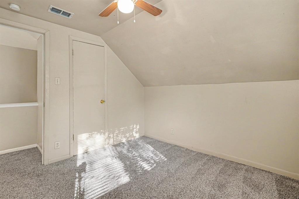 Sloped ceiling room featuring a ceiling fan with light, gray carpeting, and a closet with a gold-tone doorknob
