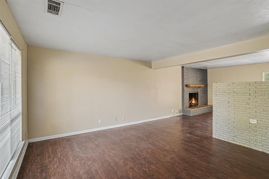 Spacious living area featuring wood-finish flooring, a full-height brick fireplace with a wood mantel, and large windows