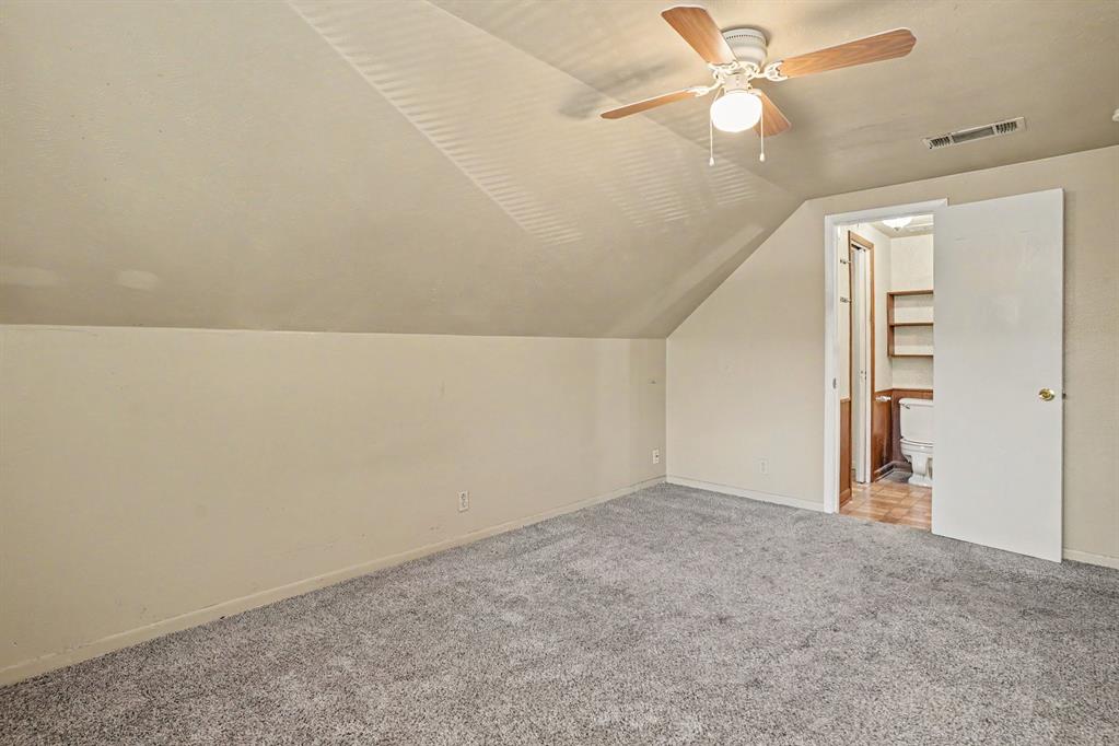 Sloped ceilings with a ceiling fan light fixture, carpeted flooring, and an adjoining room with built-in shelving