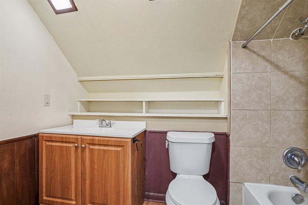 White vanity countertop, wood-finish vanity cabinetry, built-in shelving, tiled shower surround, and a skylight