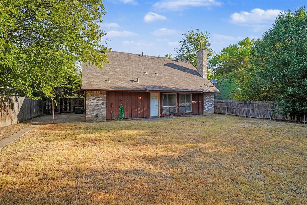 Expansive backyard featuring a partial brick and wood exterior, multiple mature trees, and a privacy fence