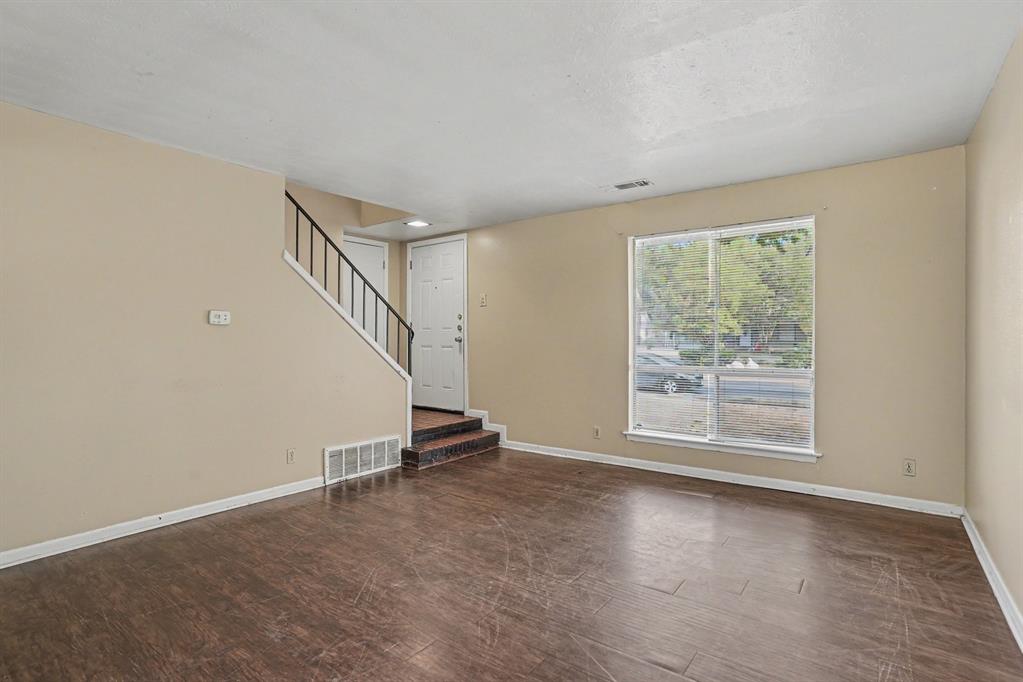 Spacious living area featuring wood-finish flooring, a large window, neutral wall tones, and a staircase with a black metal railing
