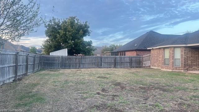 Fenced backyard with a brick exterior, shingled roof, and mature trees