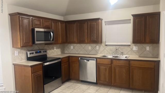 Kitchen featuring wood cabinetry, stainless steel appliances, a tiled backsplash, a double basin sink, and tile flooring