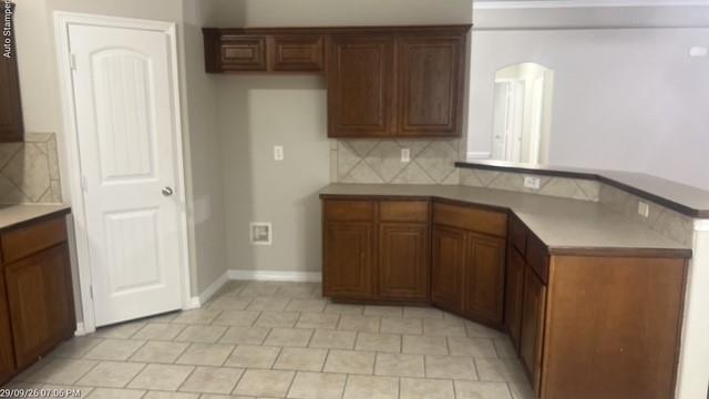 Wood-finish cabinetry, tile flooring, tile backsplash, and a multi-level countertop