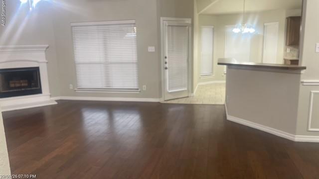 Hardwood-finish flooring, a white mantel fireplace, a large window with blinds, a built-in breakfast bar, and vaulted ceilings