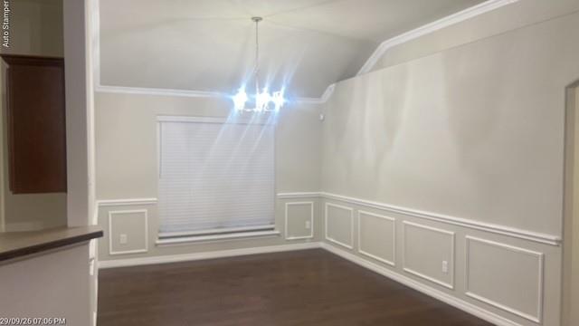 Vaulted ceiling featuring a decorative chandelier, wainscoting detailing, wood-finish flooring, and crown molding