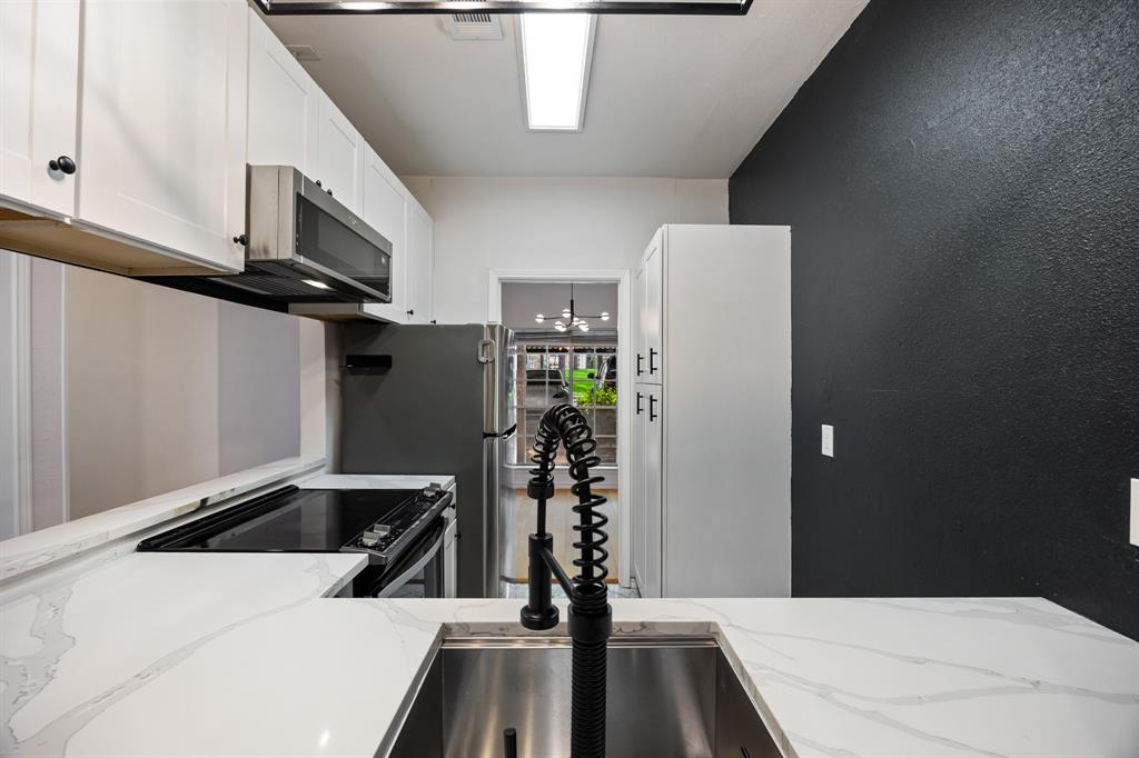 White shaker-style cabinetry with dark hardware, stainless steel appliances, white patterned countertops, stainless steel undermount sink, and a black gooseneck pull-down faucet