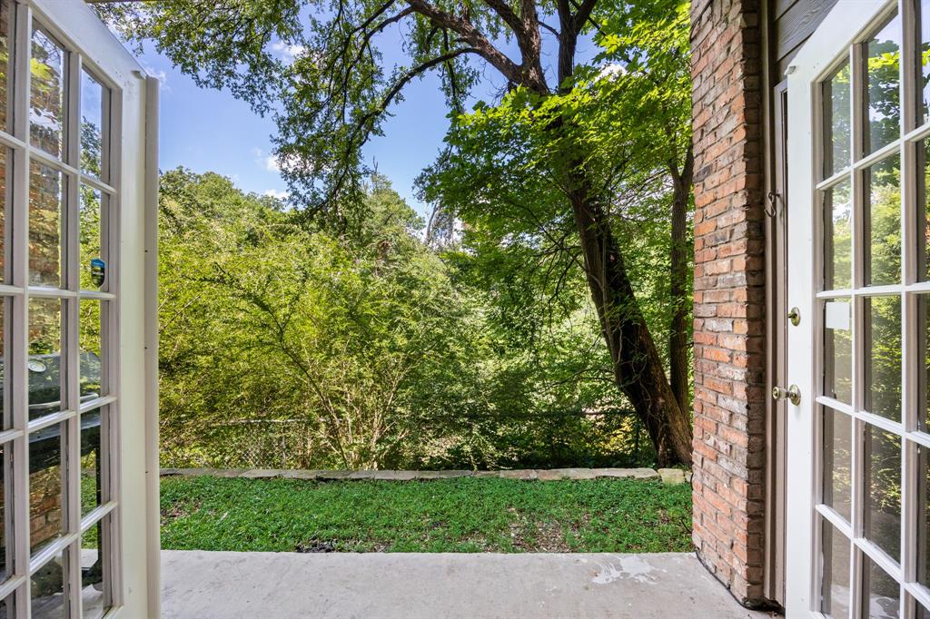 Patio with concrete flooring, brick exterior wall, and double French doors opening to a grassy area and mature trees