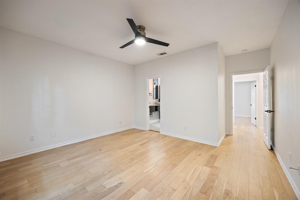 Spacious room with wood-finish flooring, a modern ceiling fan, and crisp white walls