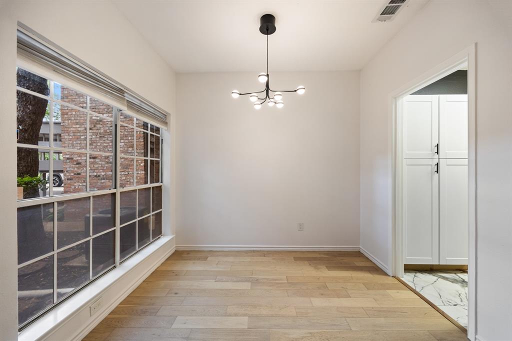 Expansive window with grid panes, wood-finish flooring, contemporary ceiling fixture, white walls, and built-in white cabinetry with black hardware