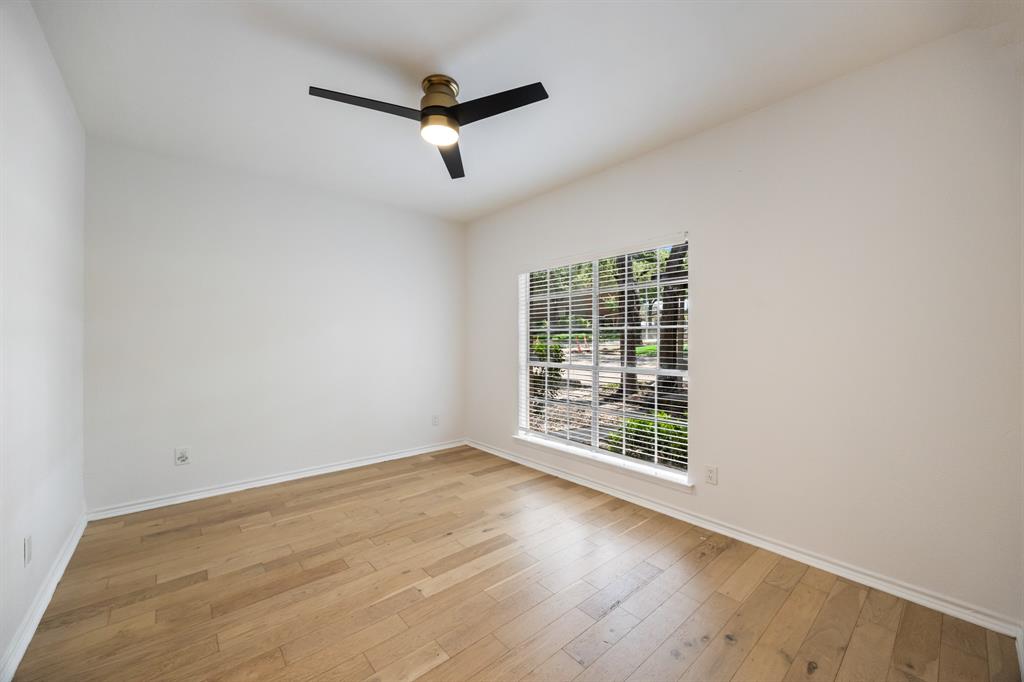 Light wood-finish flooring, white walls, and a modern ceiling fan with integrated lighting