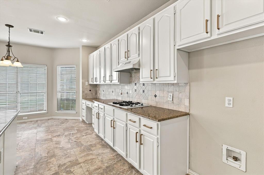 A BEAUTIFUL BLEND OF FORM AND FUNCTION! An impressive wall of freshly painted white cabinetry with brushed gold, warm granite countertops, decorative tile backsplash, and built-in gas cooktop provide generous storage and preparation space.
