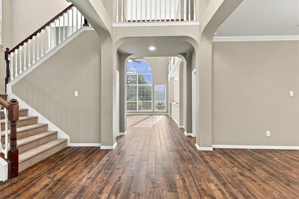 GRAND DESIGN MEETS TIMELESS STYLE! A beautiful staircase, open second-story balcony, graceful archways, and rich wood-look tile  floors showcase the home's exceptional architectural character. A light-filled passageway offers a captivating glimpse into the impressive living spaces beyond.