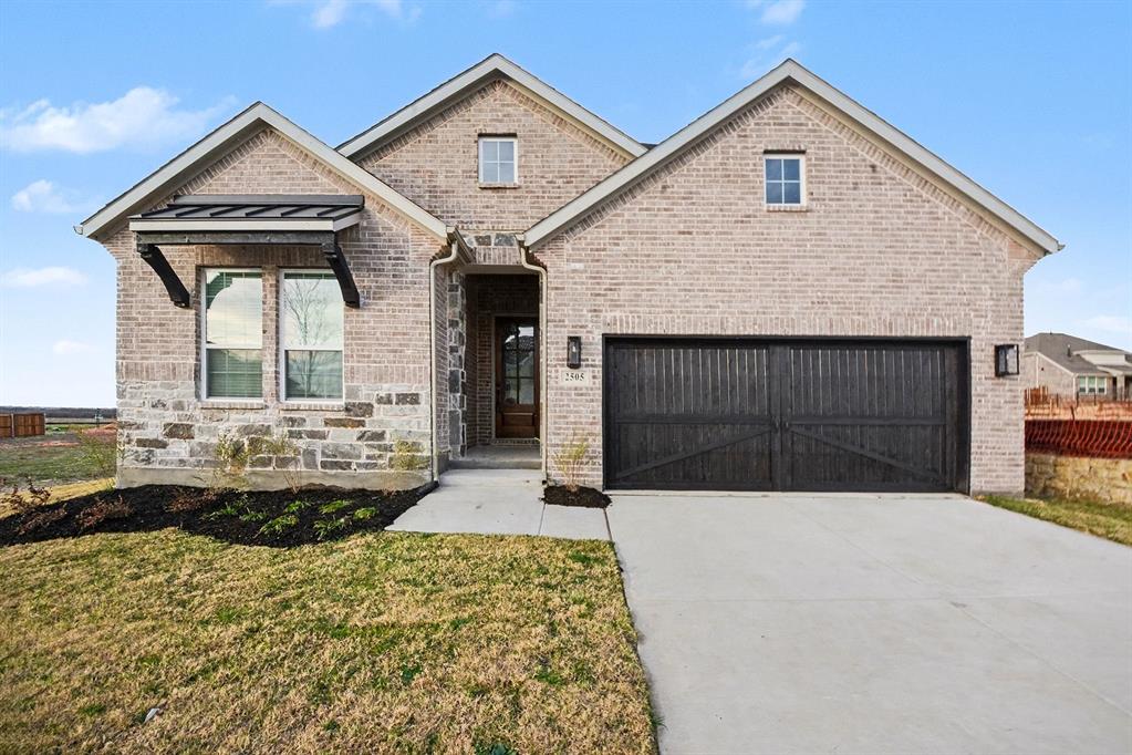 Exterior facade featuring brick masonry with stone veneer accents, multi-gabled roofline, dark metal awning, and a custom-style carriage-door garage