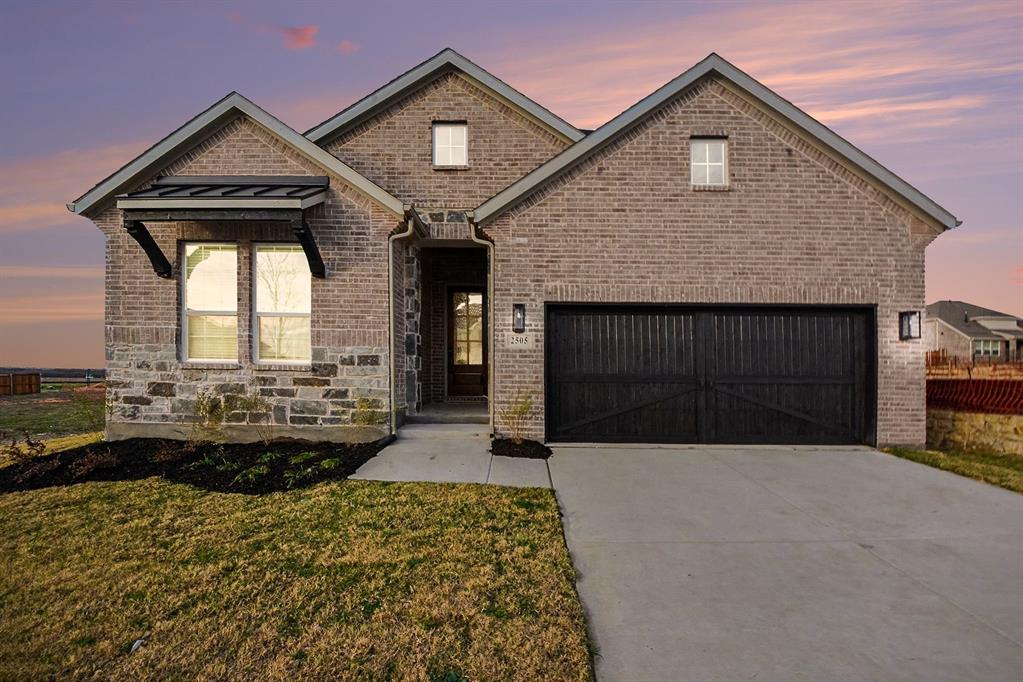 Brick and stone exterior facade featuring a covered front entryway, metal window awning, and a two-car garage with carriage-style doors Brick and stone exterior facade featuring a covered front entryway, metal window awning, and a two-car garage with carriage-style doors