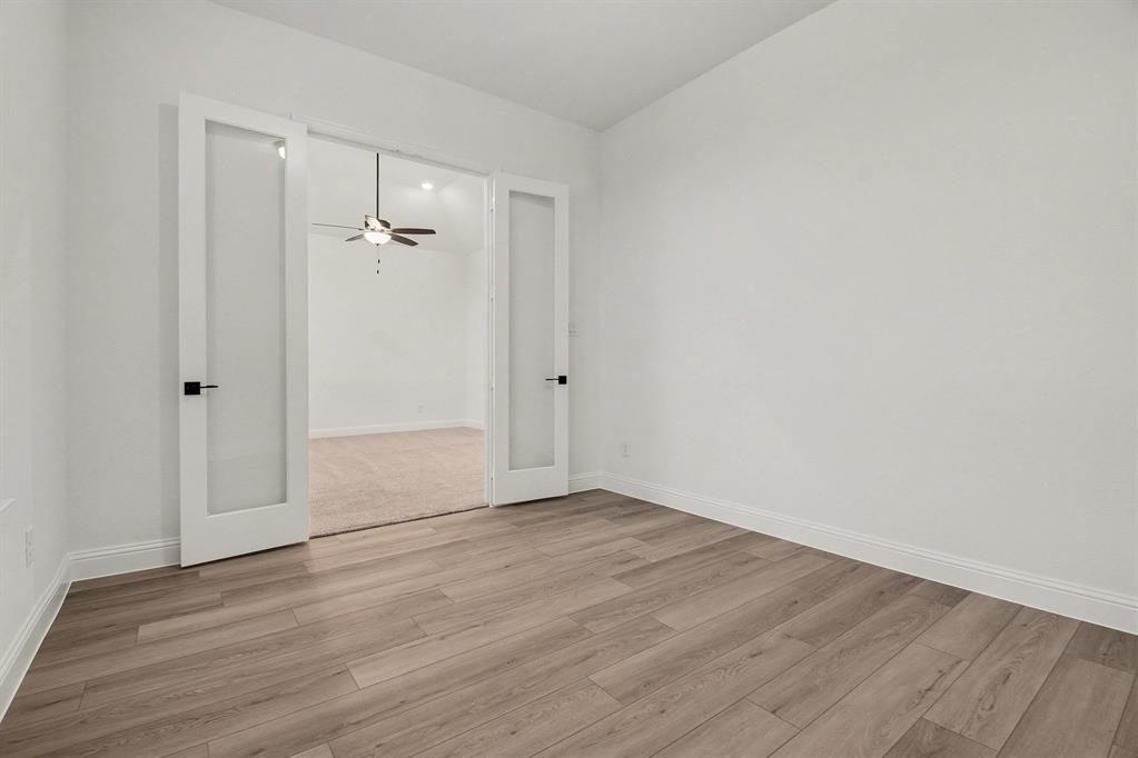 Room featuring wood-finish flooring, white walls, and white French doors with glass panels and matte black hardware