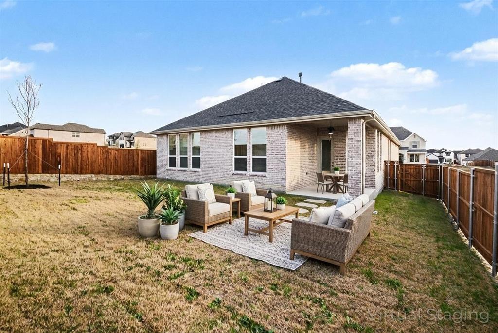 Rear elevation featuring light-toned brick masonry, a covered concrete patio, multi-pane windows, and a fully enclosed wood privacy fence