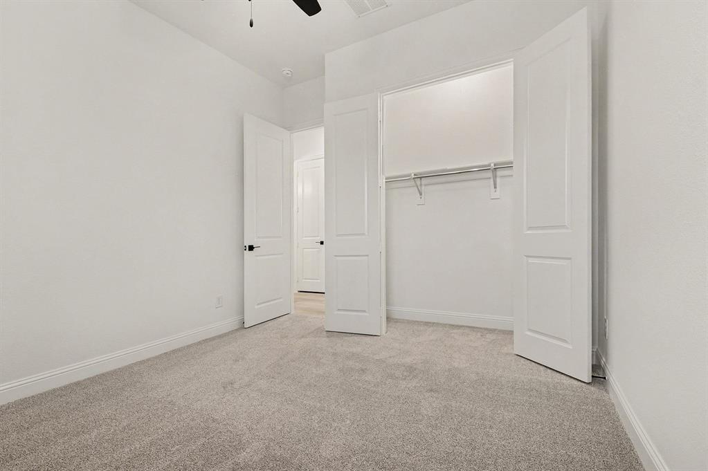 Neutral-toned carpeting, two-panel interior doors with matte black hardware, and a reach-in closet featuring a built-in metal shelving rod